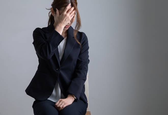 手で顔を覆うスーツ姿の女性。