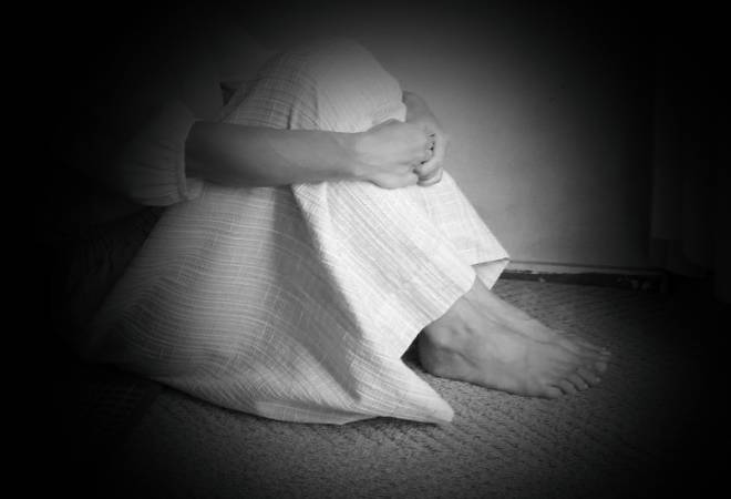 膝を抱え蹲る女性のモノクロ写真。