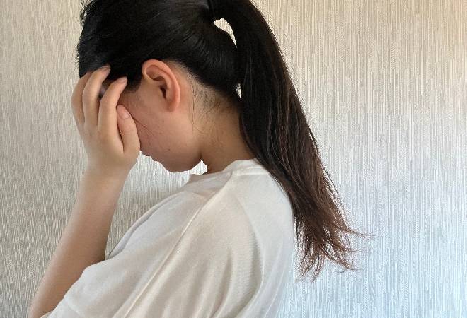 頭を抱え悩む母親の後ろ姿。